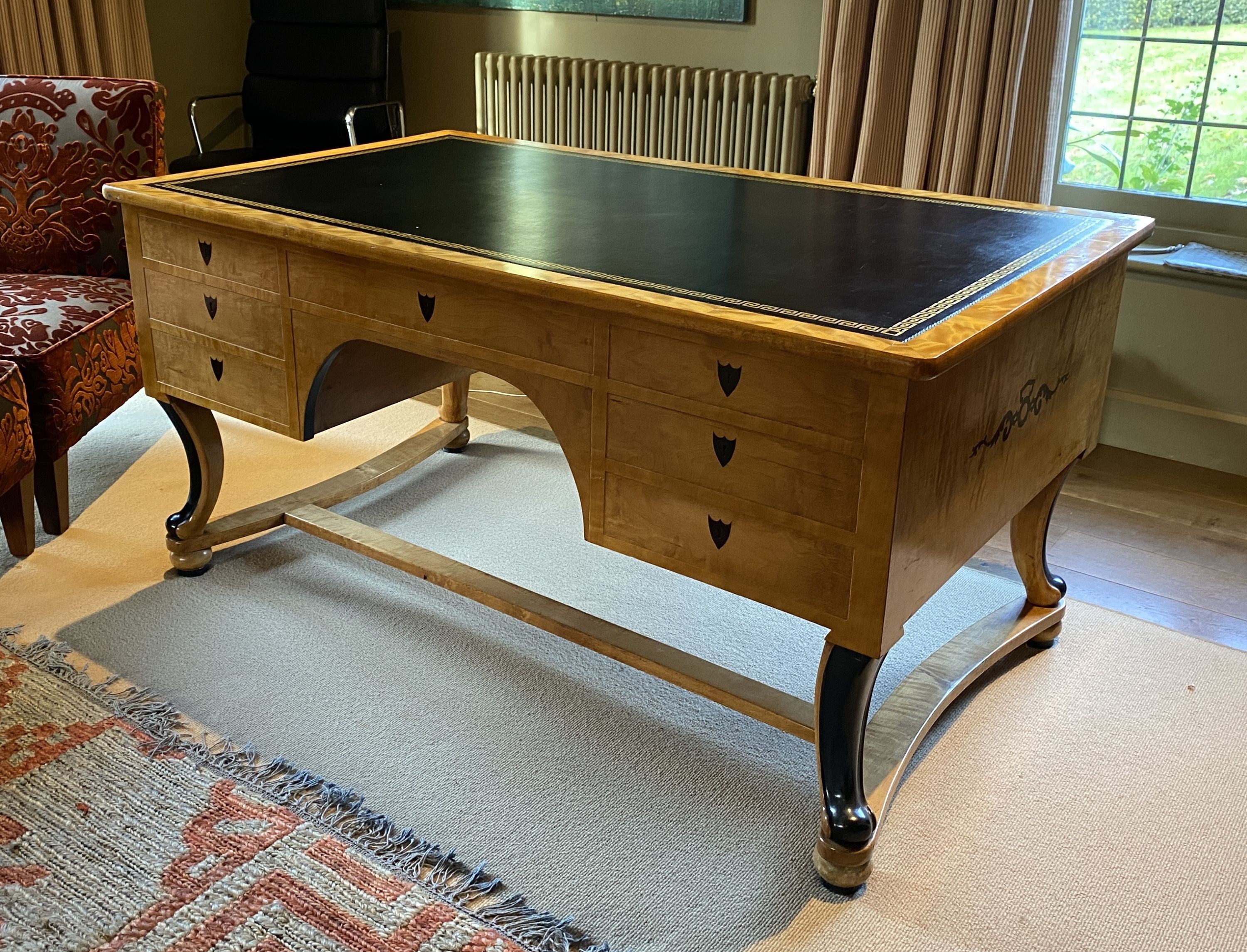 A Biedermeier style maple desk, with black leather skiver and seven drawers, on ebonised scroll legs with H stretcher, width 155cm depth 91cm height 76cm